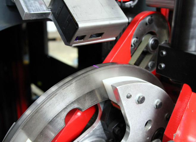 Close-up of a laser sensor scanning a rotating steel component on the machine.